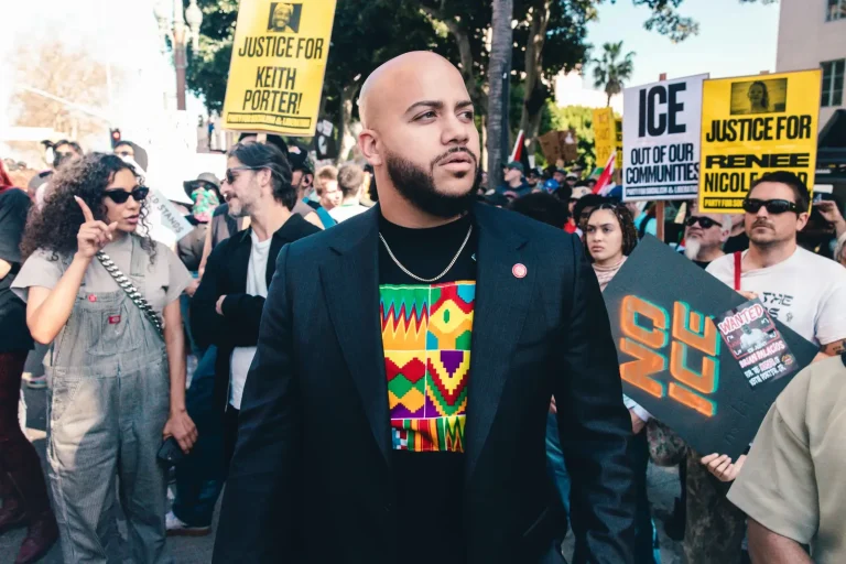 Isaac Bryan moving through a dense crowd of protesters, a hand-painted ‘No ICE’ placard and yellow printed signs held up on either side of him.